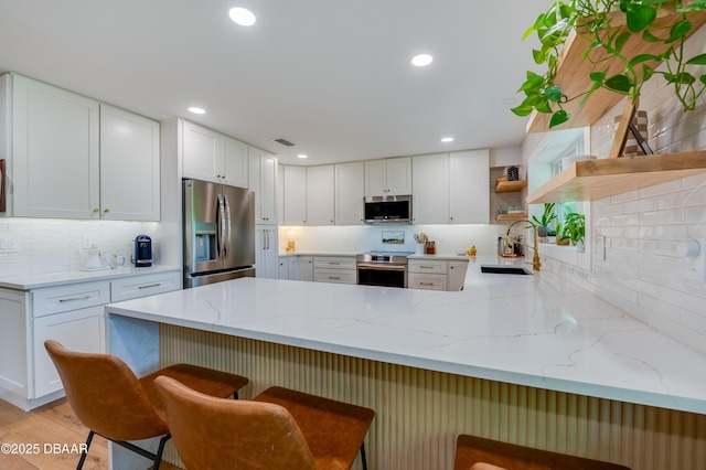kitchen with a sink, a peninsula, stainless steel appliances, open shelves, and decorative backsplash