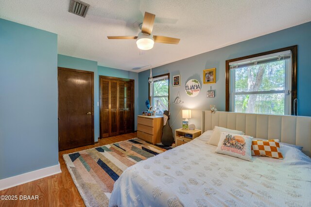 bedroom with a ceiling fan, multiple closets, a textured ceiling, visible vents, and light wood-style floors