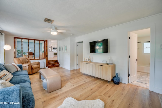 living area featuring a ceiling fan, light wood-style floors, crown molding, and visible vents