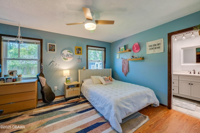 bedroom with a ceiling fan, baseboards, ensuite bath, a sink, and light wood-type flooring