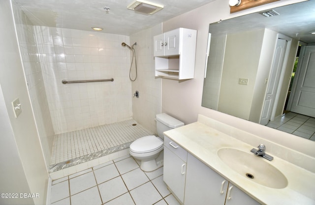 bathroom featuring tile patterned flooring, a tile shower, vanity, and toilet