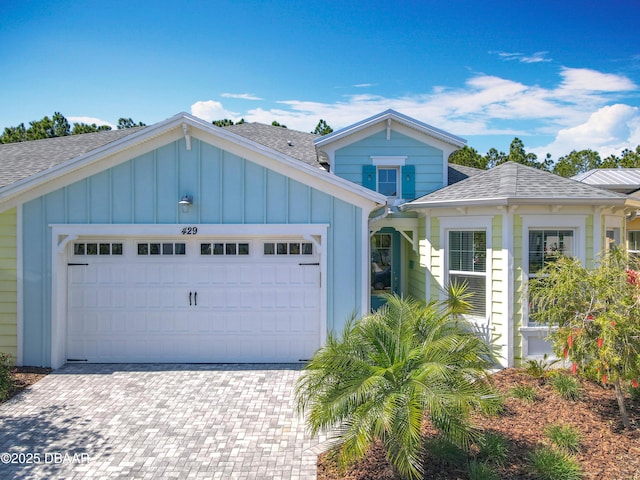 view of front of property featuring board and batten siding, a shingled roof, decorative driveway, and a garage