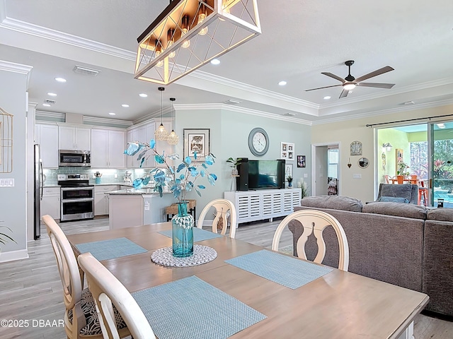 dining area with light wood-style flooring, a raised ceiling, ornamental molding, and a ceiling fan