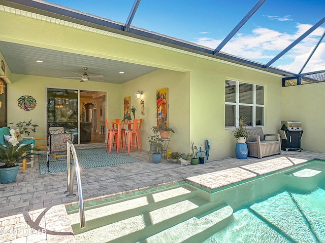 outdoor pool featuring glass enclosure, a patio, a ceiling fan, and a grill