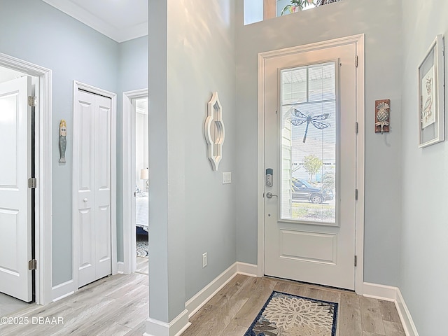 entrance foyer with light wood-type flooring, baseboards, and crown molding