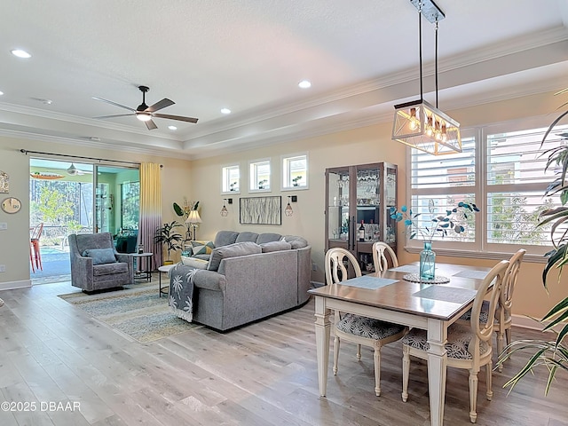 dining room with light wood-style flooring, ornamental molding, a ceiling fan, a tray ceiling, and recessed lighting