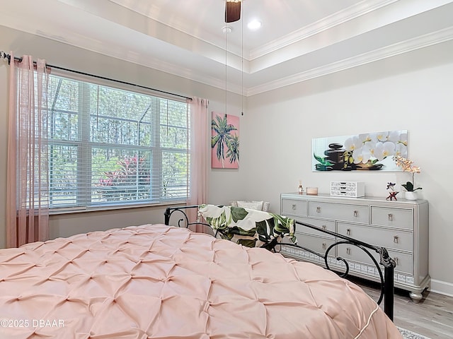 bedroom with crown molding, wood finished floors, baseboards, and a tray ceiling