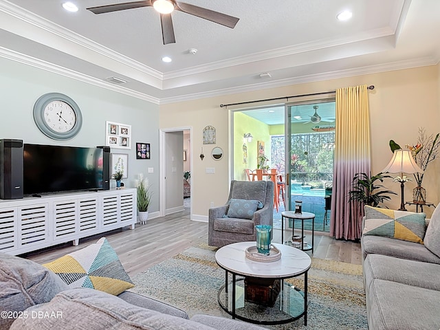 living area with crown molding, baseboards, wood finished floors, a raised ceiling, and a ceiling fan