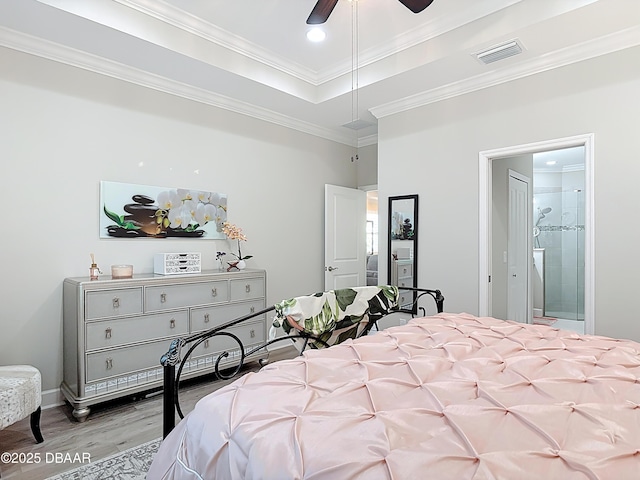 bedroom featuring visible vents, ensuite bath, light wood-style flooring, crown molding, and a raised ceiling