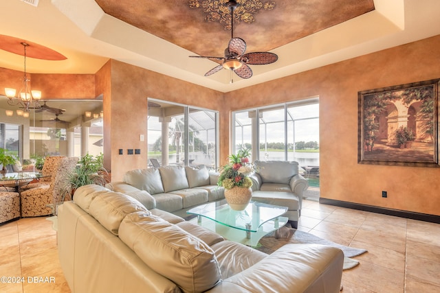 tiled living room featuring ceiling fan with notable chandelier, a water view, and a tray ceiling