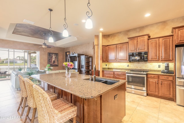 kitchen featuring stainless steel appliances, ceiling fan, sink, a center island with sink, and hanging light fixtures