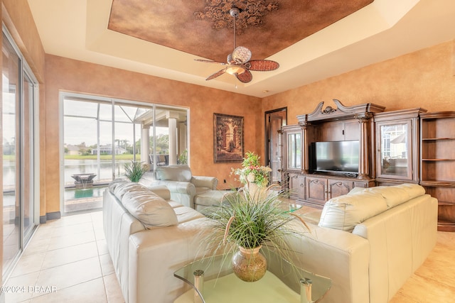 tiled living room featuring a water view, a raised ceiling, and ceiling fan