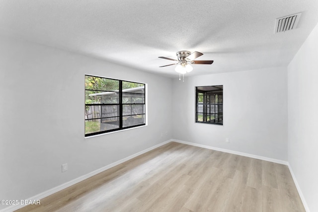 empty room with a textured ceiling, a ceiling fan, baseboards, light wood-type flooring, and visible vents