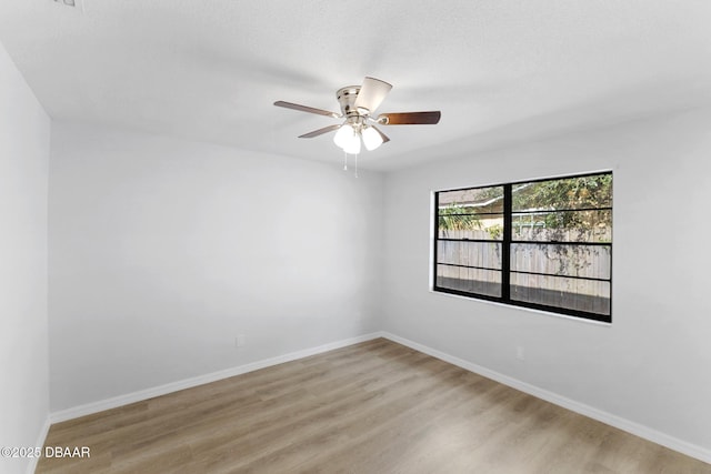 spare room featuring light wood-style floors, a ceiling fan, and baseboards