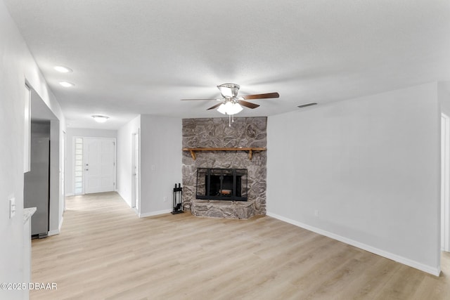 unfurnished living room with a ceiling fan, visible vents, a fireplace, baseboards, and light wood-style floors