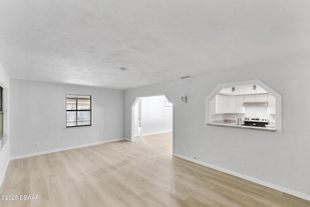 unfurnished living room featuring visible vents, arched walkways, light wood-type flooring, a sink, and baseboards