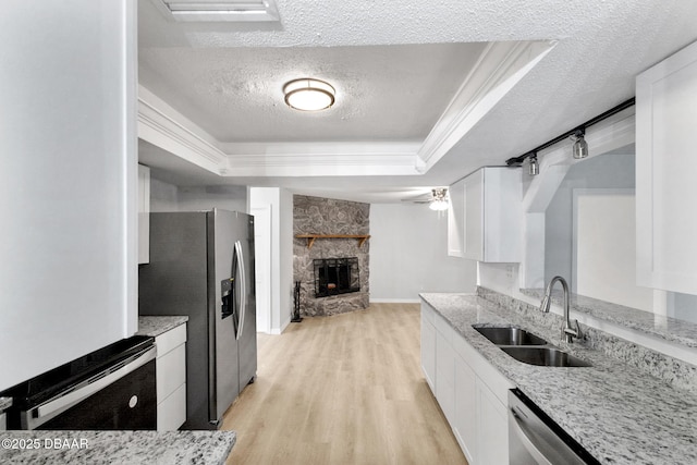 kitchen with a sink, light wood-style floors, a textured ceiling, white cabinetry, and a tray ceiling
