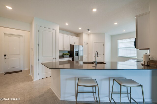 kitchen with white cabinetry, stainless steel fridge with ice dispenser, sink, a breakfast bar, and kitchen peninsula