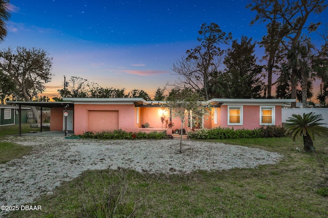 back of house at dusk with driveway, a lawn, an attached garage, and stucco siding