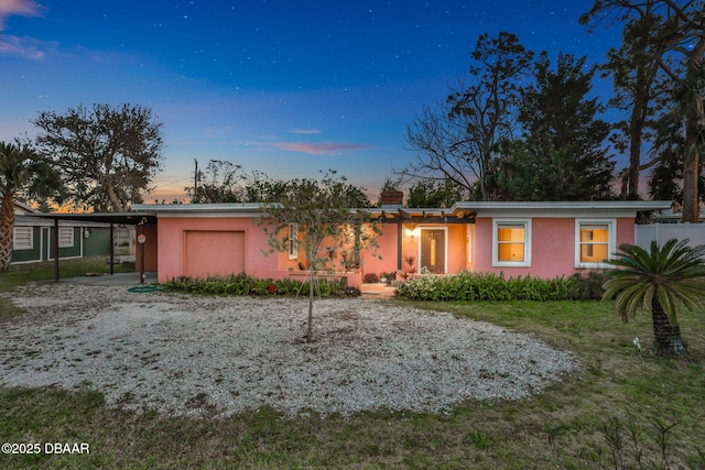 back of house at dusk with an attached garage, driveway, and stucco siding