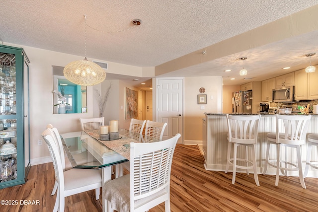 dining room featuring light wood finished floors, visible vents, baseboards, a textured ceiling, and recessed lighting