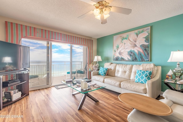 living room with a textured ceiling, ceiling fan, a water view, and wood finished floors