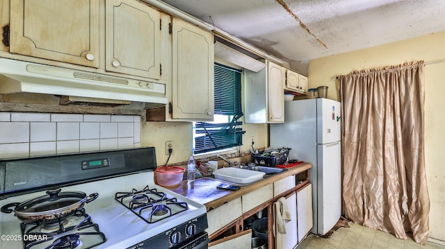 kitchen featuring white fridge, cream cabinets, gas stove, and decorative backsplash