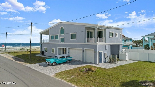 rear view of house featuring a lawn, a garage, a balcony, and a water view