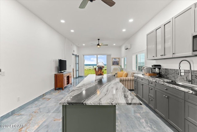 kitchen featuring a wall mounted air conditioner, sink, gray cabinets, a kitchen island, and light stone counters