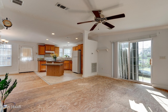 kitchen featuring visible vents, a kitchen island, brown cabinets, open floor plan, and freestanding refrigerator