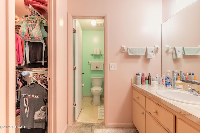 bathroom with vanity, a walk in closet, toilet, and baseboards