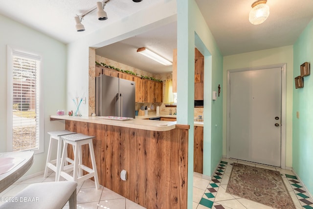 kitchen with a breakfast bar, light countertops, light tile patterned floors, decorative backsplash, and high end refrigerator