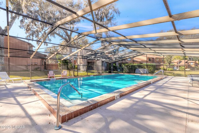 community pool with a patio area, glass enclosure, and fence