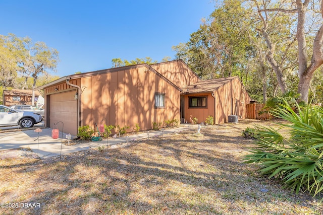 view of front facade with driveway, fence, board and batten siding, a garage, and central AC unit