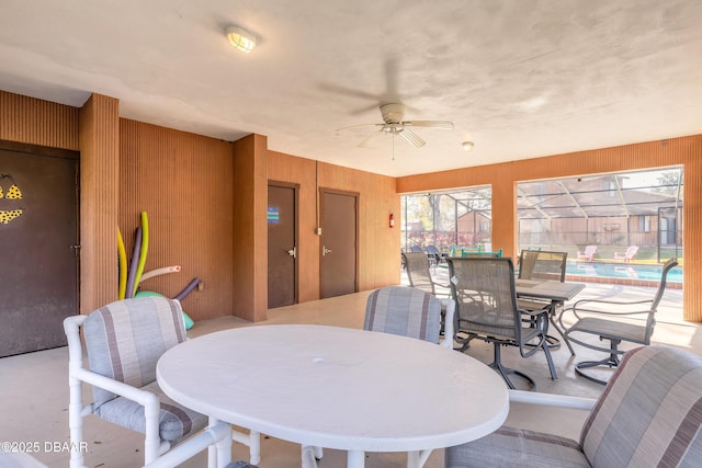 dining space with wood walls, a ceiling fan, and a sunroom