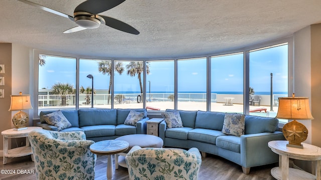 living room featuring ceiling fan, a beach view, a textured ceiling, a water view, and hardwood / wood-style flooring