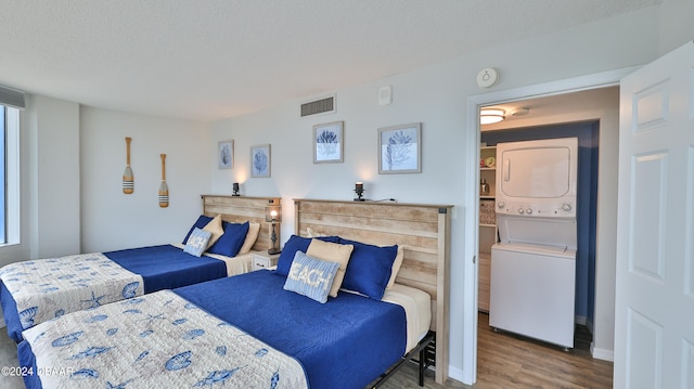 bedroom with hardwood / wood-style floors, a textured ceiling, and stacked washing maching and dryer