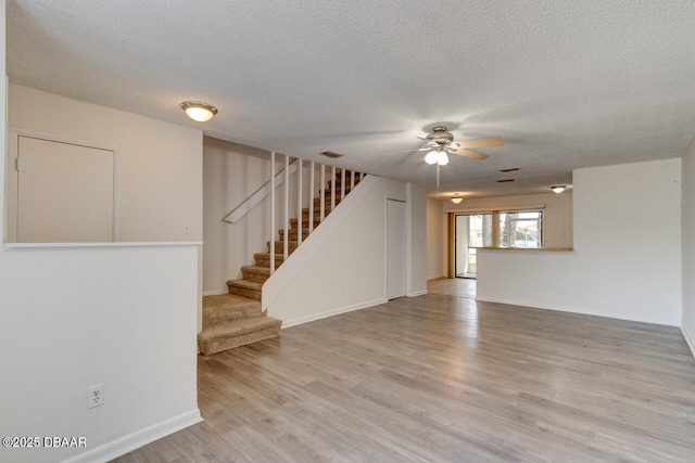 188 W Sandalwood Ct, Daytona Beach, FL 32119 - unfurnished living room with light wood-style flooring, a textured ceiling, a ceiling fan, and stairway