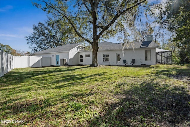 rear view of property featuring a yard, glass enclosure, and central air condition unit