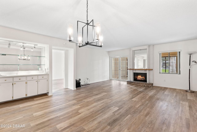 unfurnished living room featuring a fireplace, an inviting chandelier, a textured ceiling, and light wood-type flooring