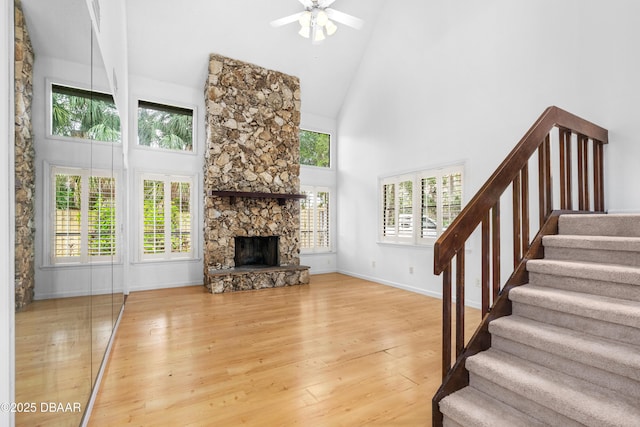 living room featuring ceiling fan, hardwood / wood-style flooring, a stone fireplace, and high vaulted ceiling