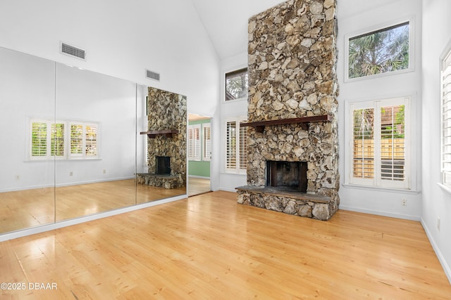 unfurnished living room featuring high vaulted ceiling, a stone fireplace, and light wood-type flooring