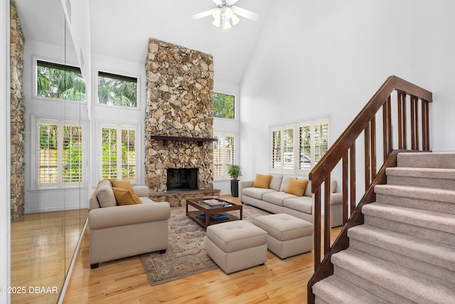 living room featuring ceiling fan, light hardwood / wood-style flooring, a healthy amount of sunlight, a stone fireplace, and high vaulted ceiling