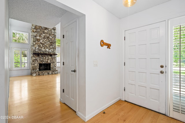 foyer entrance featuring a textured ceiling, a wealth of natural light, hardwood / wood-style flooring, and a stone fireplace