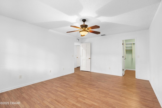 empty room with ceiling fan, light wood-type flooring, and a textured ceiling