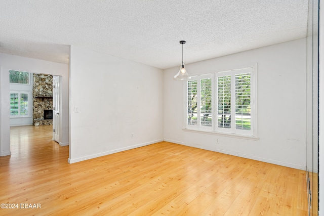 spare room featuring a textured ceiling, hardwood / wood-style flooring, and a stone fireplace