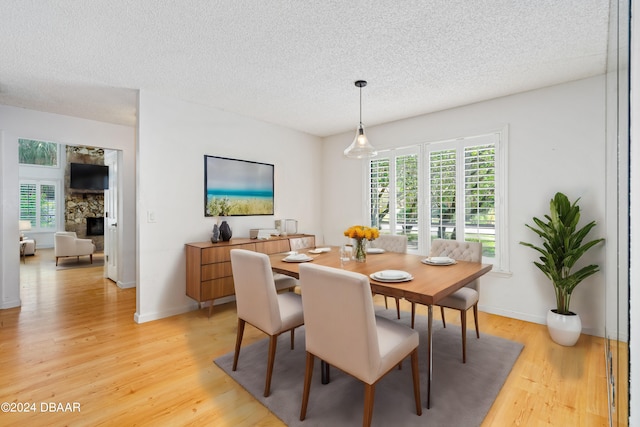 dining space featuring a stone fireplace, a textured ceiling, and light hardwood / wood-style floors