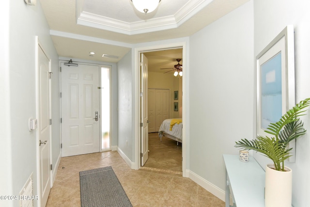 tiled foyer entrance featuring ceiling fan, a tray ceiling, and ornamental molding