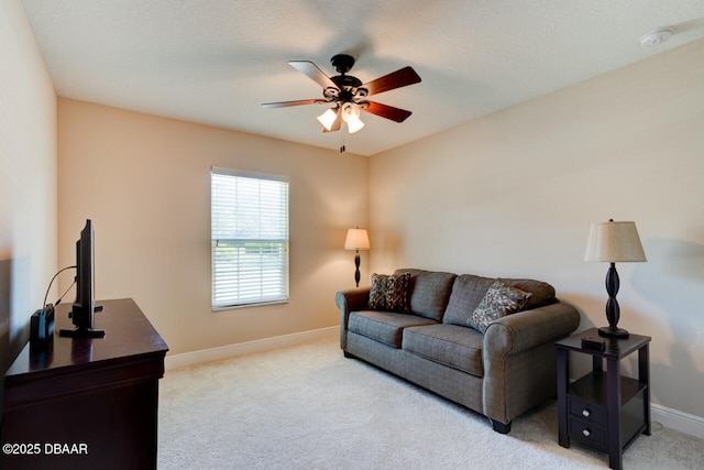 living area featuring baseboards, a ceiling fan, and light colored carpet