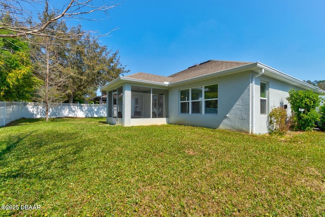 rear view of property featuring a sunroom, roof with shingles, fence, a yard, and stucco siding